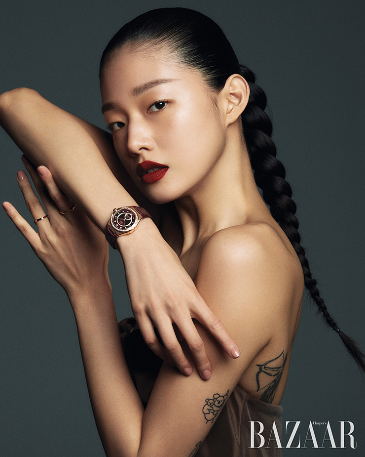 다이아몬드가 세팅된 베젤과 버건디 다이얼로 시선을 사로잡는 ‘컨스텔레이션 코-액시얼 크로노미터 스몰 세컨즈 34mm’ 워치, 왼손 검지에 착용한 ‘컨스텔레이션’ 링과 약지에 ‘아쿠아 스윙 와이드 웨이브’ 링은 Omega. 오프숄더 톱은 Totême.