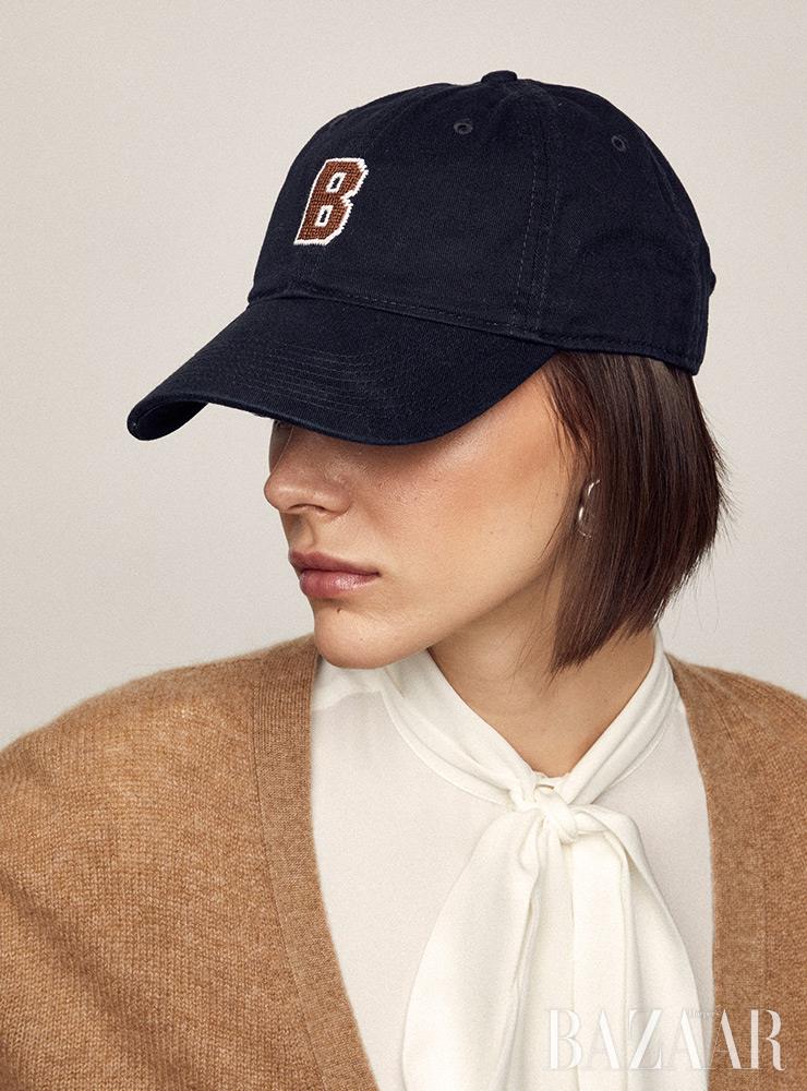 볼캡은 J. Press. 카디건은 Khaite. 타이 블라우스는 Polo Ralph Lauren. 귀고리는 Ben-Amun by Isaac Manevitz.