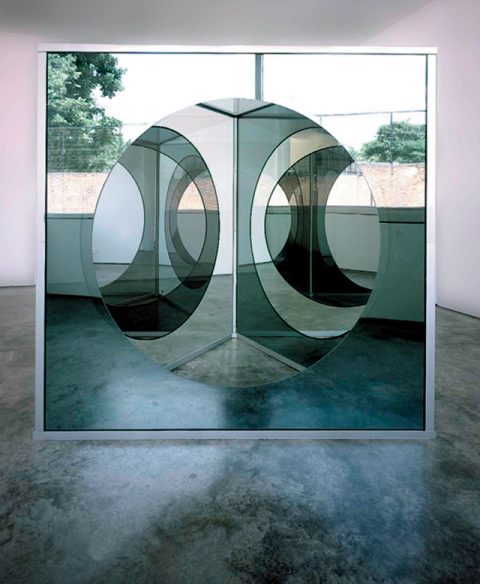 GRAD010001 Dan Graham,‘Triangular Pavilion with Circular Cut-Out Variation C’, 1989~2001,Two Way Mirror Glass, Plain Glass, Painted Aluminium and Stainless Steel205×208cm80.7×81.9in© Dan Graham; Courtesy Lisson Gallery