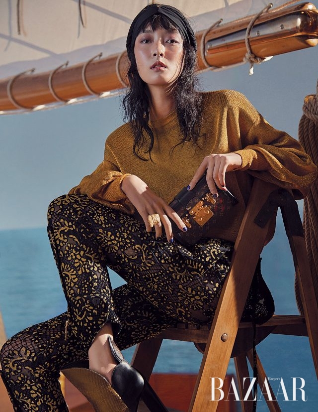 골드 니트 스웨터, 레이스 팬츠, 메탈릭 부츠, 트렁크 형태의 미니 클러치 백은 모두 Louis Vuitton 제품.