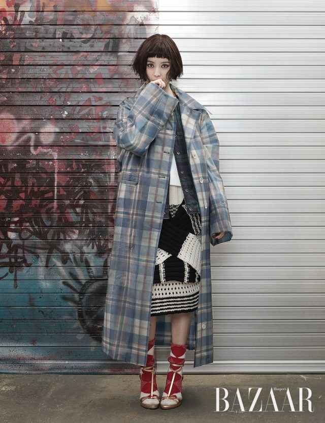 타탄체크 패턴의 레인코트, 리버서블이 가능한 체크 퀼팅 베스트, 이너로 입은 화이트 톱, 스웨터를 허리에 두른 듯한 디테일의 니트 스커트, 아가일 체크 양말, T 스트랩 힐은 모두 Burberry 제품.