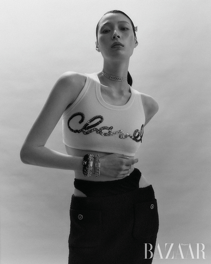 로고 장식의 탱크톱, 컷아웃 스커트, 헤어핀, 초커, 팔에 레이어드한 스크런치는 모두 Chanel.