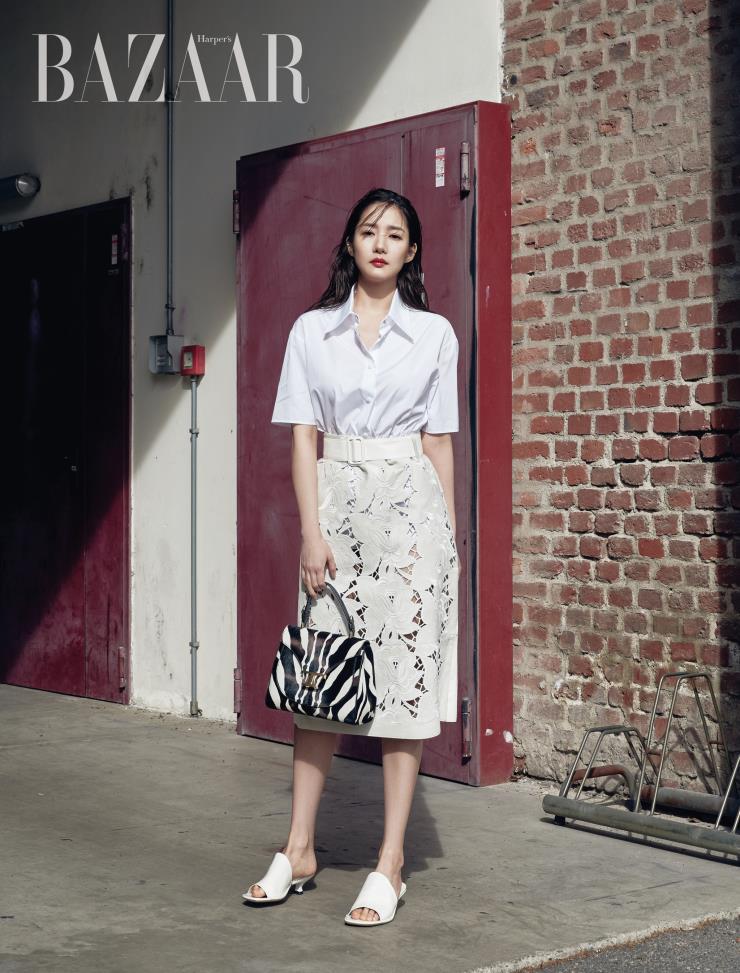 화이트 셔츠, 스커트, 지브러 패턴의 ‘타임리스 T’ 토트백, 뮬은 모두 Tod’s.