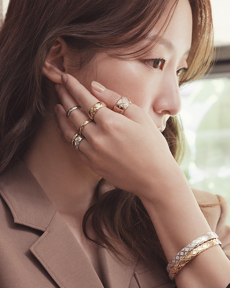 엄지에 착용한 베이지 골드 다이아몬드 라지 링, 검지에 착용한 옐로 골드 스몰 링, 중지에 착용한 화이트 골드 미니 링, 옐로 골드 미니 링, 약지에 착용한 옐로 골드 미니 링, 화이트 골드 스몰 링, 화이트 골드에 다이아몬드가 세팅된 브레이슬릿, 옐로 골드 브레이슬릿은 모두 Chanel CoCo Crush.